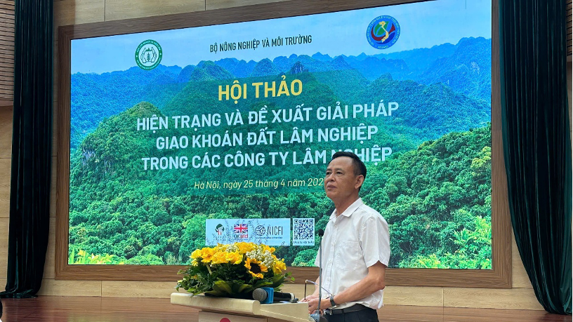 Một diễn giả đang phát biểu tại hội thảo về giải pháp giao khoán đất lâm nghiệp, với màn hình lớn phía sau hiển thị thông tin sự kiện.